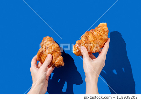 Women's hands hold fresh croissants on a blue background. Design concept for breakfast  118939202