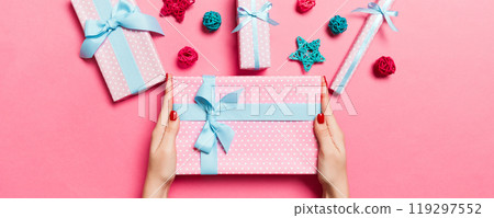 Top view of female hands holding a Christmas present on festive pink background. Holiday decorations, toys and balls. New Year holiday concept 119297552