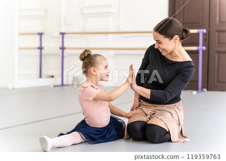 Little girl sitting on studio floor with her teacher clapping after ballet lesson 119359763