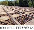 Wide-angle view of roof framing with wooden beams and connector plates, capturing the scale and structure under a clear sky 119366312