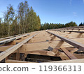 Roof framing in progress with a view of forest in the background, showcasing the orderly alignment of wooden trusses under a clear blue sky 119366313