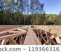 Overhead perspective of roof trusses and beams on a construction site surrounded by trees, emphasizing the natural setting and structural layout 119366316