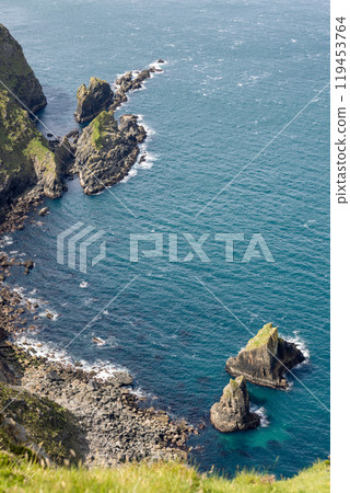 Aerial shot of rugged rocks protruding from the ocean at Slieve League, Ireland, with steep cliffs and clear blue water surrounding the shoreline 119453764