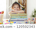 Smiling child under book roof at desk 120502343