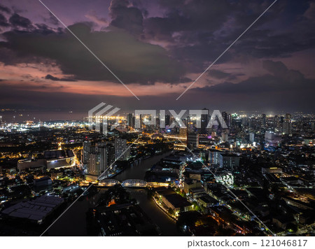 Manila's city lights shimmering at dusk, forming a stunning vista beneath a dramatic sky, displaying lively urban scenery from an elevated perspective 121046817