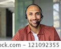 Happy customer service agent with headset providing assistance remotely. Confident professional delivering excellent support in modern office setting with friendly demeanor. 121092355