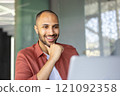 Smiling man wearing casual shirt engaged with laptop, reflecting modern work lifestyle. Person looks happy and focused during video call or virtual meeting, showcasing remote work culture. 121092358