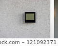 Electronic thermostat mounted on white wall displaying current indoor temperature. Device is sleek, modern, and essential for climate control in a minimalist environment. 121092371