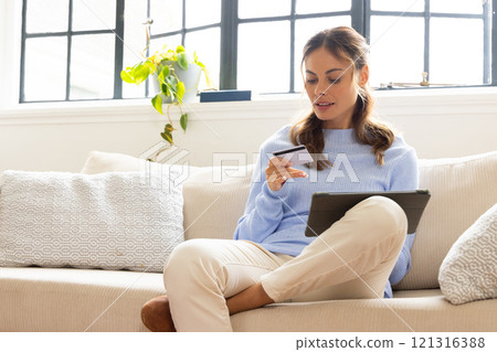 Woman shopping online using tablet and credit card, sitting on cozy sofa, at home 121316388