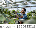 Young bearded man working with plants in a greenhouse 122035518