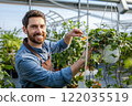 Young bearded man working with plants in a greenhouse 122035519