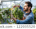 Young bearded man working with plants in a greenhouse 122035520