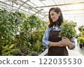 Dark-haired young woman in apron looking happy while holding a pot with flower 122035530