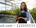 Dark-haired young woman in apron looking happy while holding a pot with flower 122035533