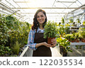 Dark-haired young woman in apron looking happy while holding a pot with flower 122035534