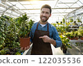 Young bearded man holding a potted flower and looking contented 122035536