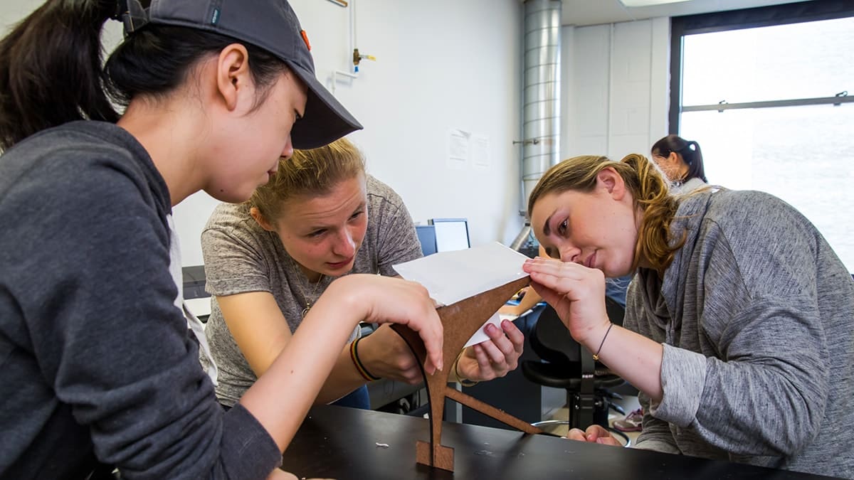 Three students look closely at a model of an architectural structure.