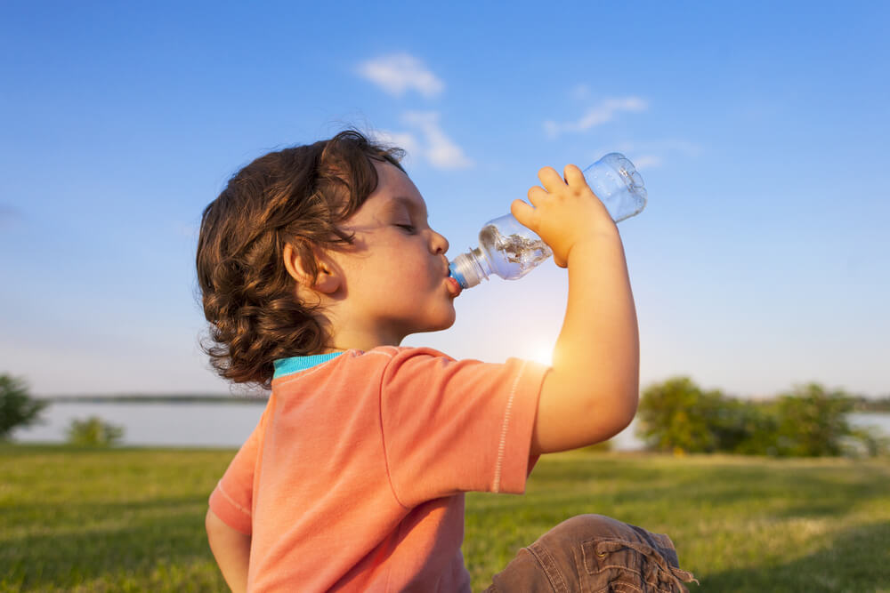 Niño bebiendo agua al aire libre.