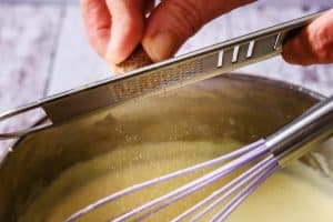 Grating nutmeg into the pan of sauce