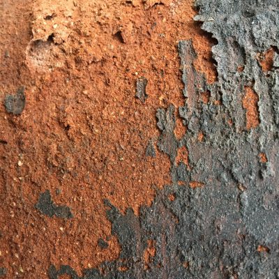 Speckled brown/red clay pot with sand like texture and crumbling charcoal grey glaze