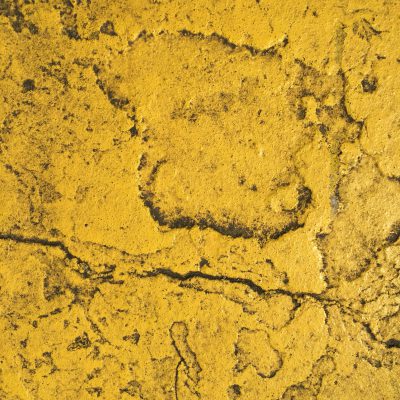 Layers of yellow paint on a concrete street with a layer of filth on top