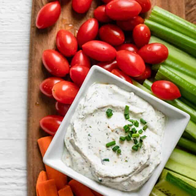 Square bowl or homemade ranch dip topped with fresh chives and surrounded by fresh vegetables