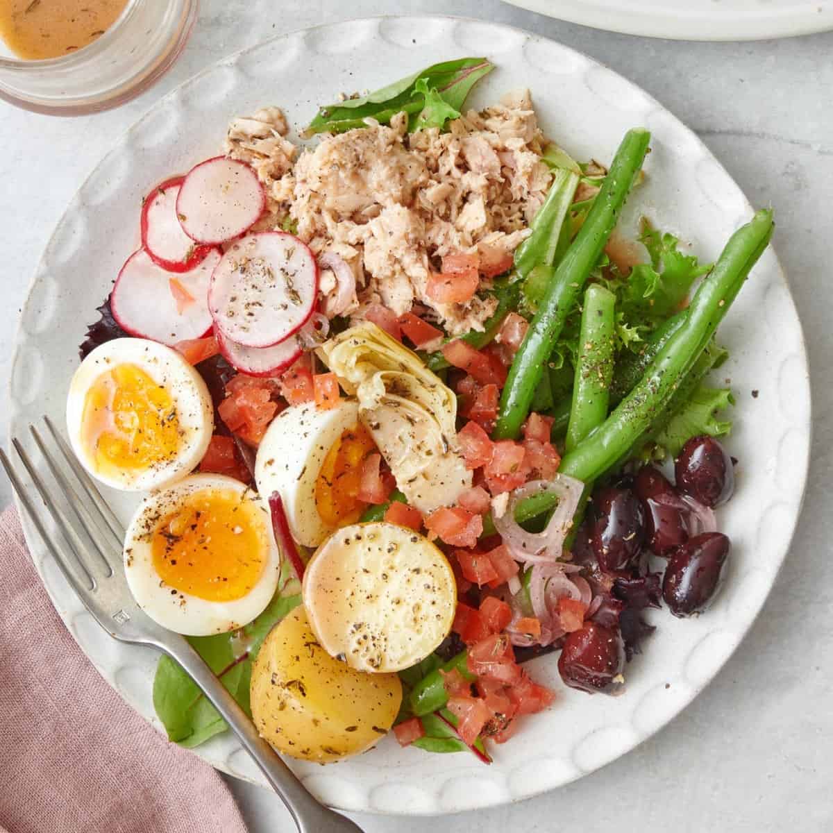 Tuna nicoise salad on a small plate with a fork.