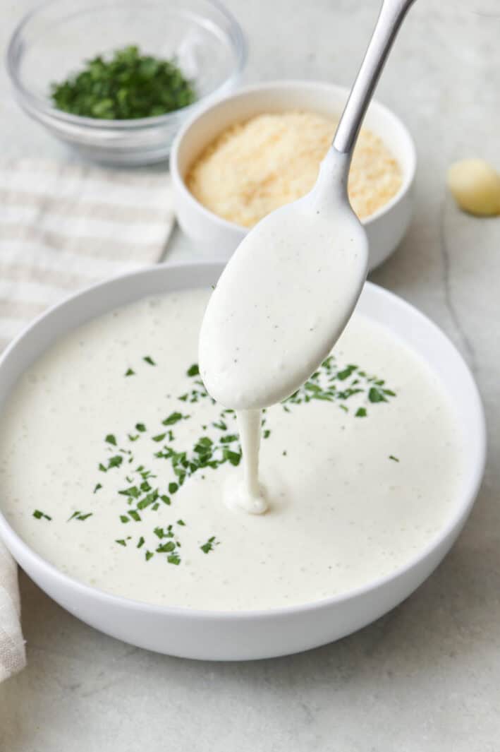 Spoon drizzling healthy alfredo sauce back into bowl.