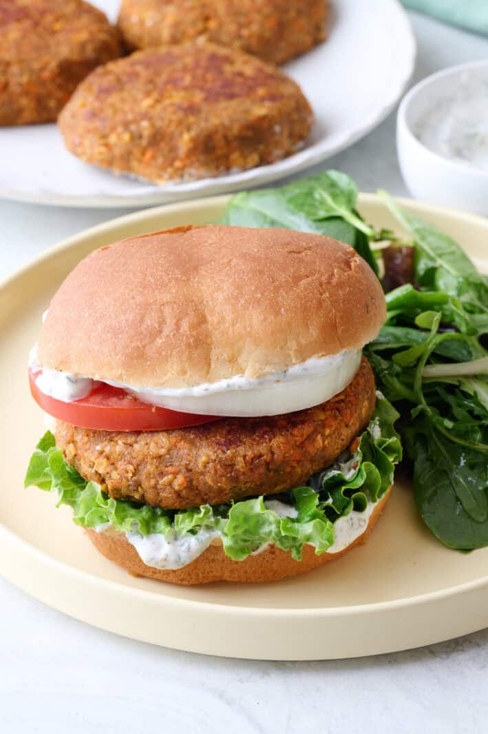 Vegetarian lentil burger on bun with toppings and sauce on a plate with a small spring salad.