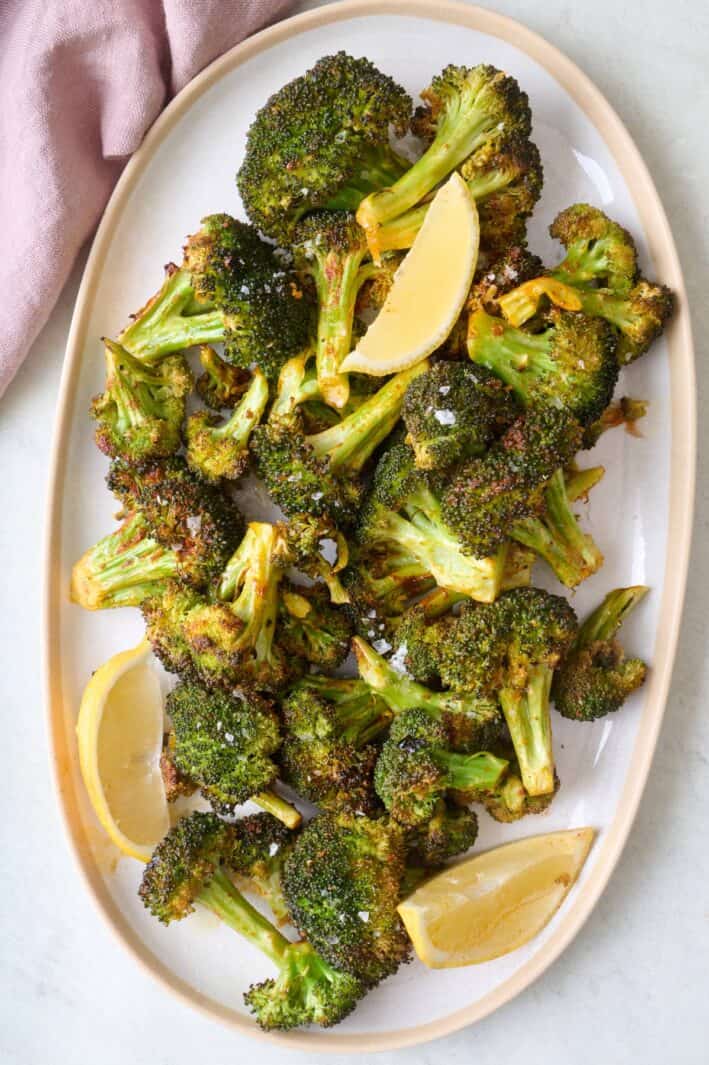 Roasted broccoli on a platter garnished with flaky salt and lemon wedges.