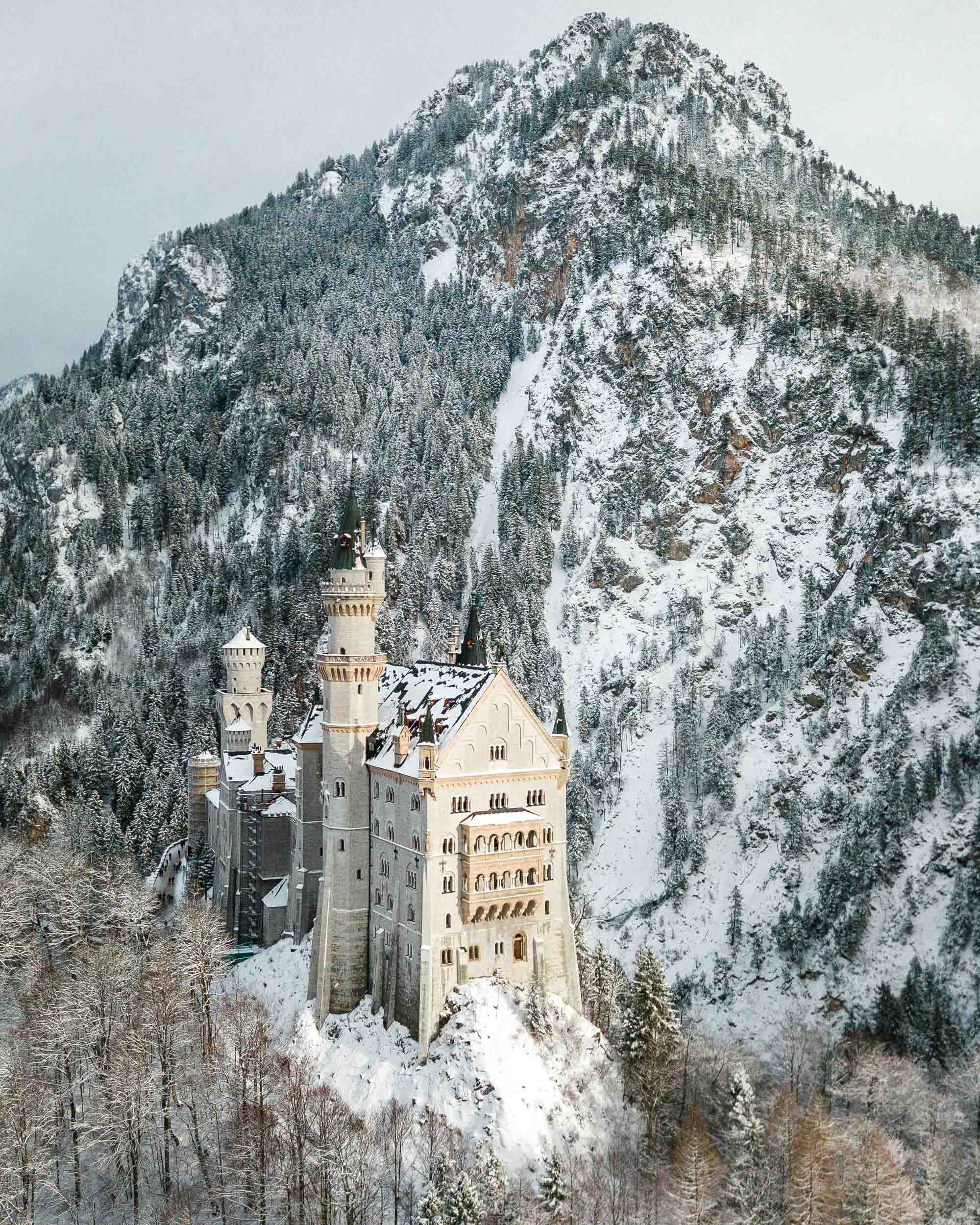 Neuschwanstein Castle in the snow in winter with mountains behind best spots to photograph german fairytale castle