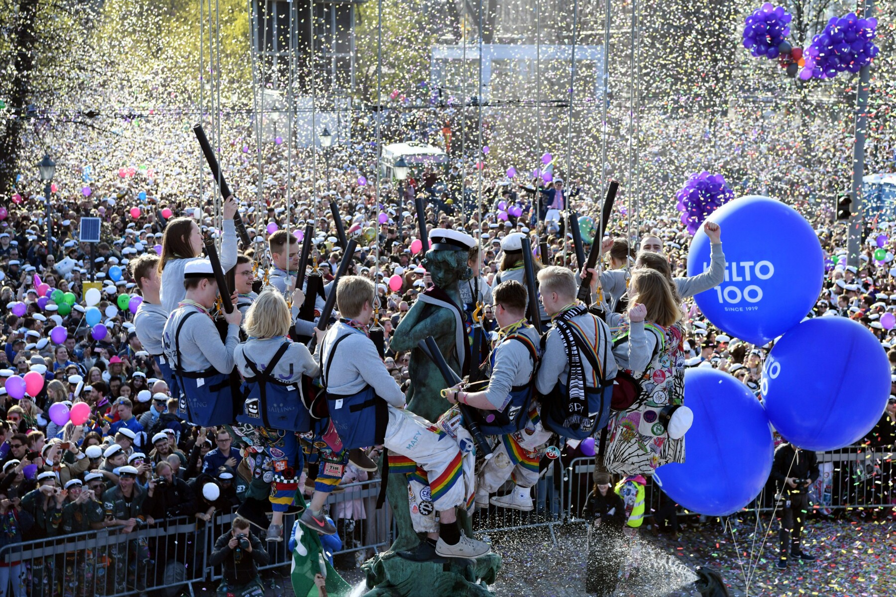 A circle of people, hanging in harnesses attached to ropes, surrounds the top of a statue of a woman, while a crowd watches from the ground.