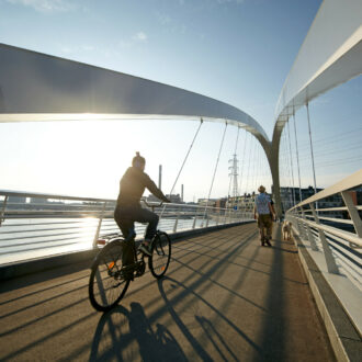 A person bikes over a bridge with the sun and the sea in the background.