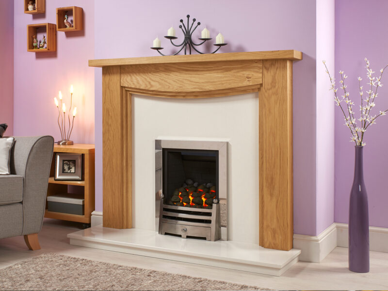 Arched stepped oak fire surround in light oiled oak against a purple wall, fitted with a white marble set and silver gas fire.