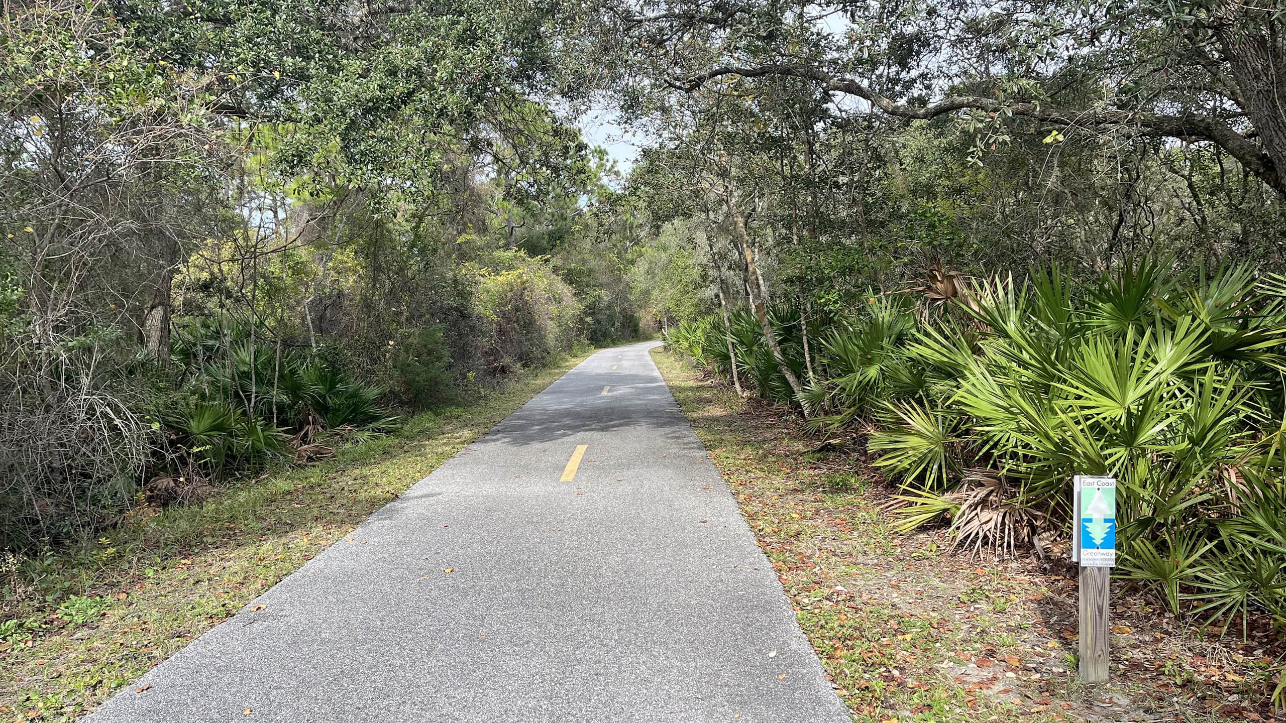 Paved path under canopy of oaks with East Coast Greenway sign