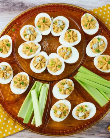 Buffalo Deviled Eggs garnished with blue cheese and sliced green onion served on a deviled egg plate.