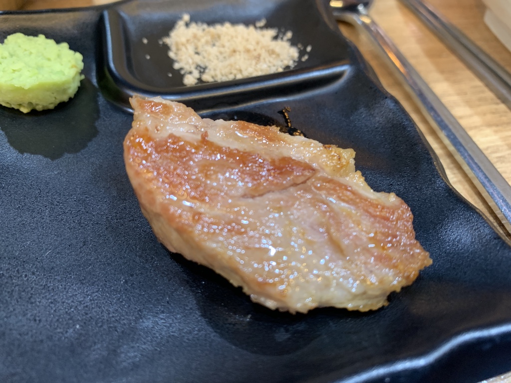 a piece of meat on a black plate with chopsticks