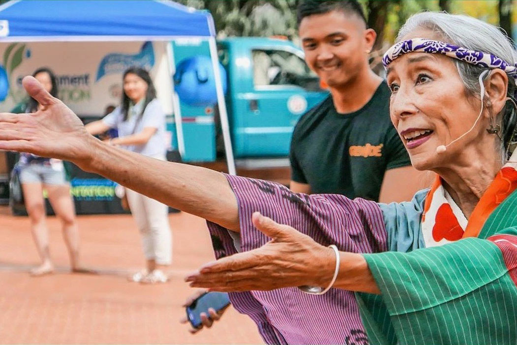 A woman dances outdoors in colorful kimono and headwrap.