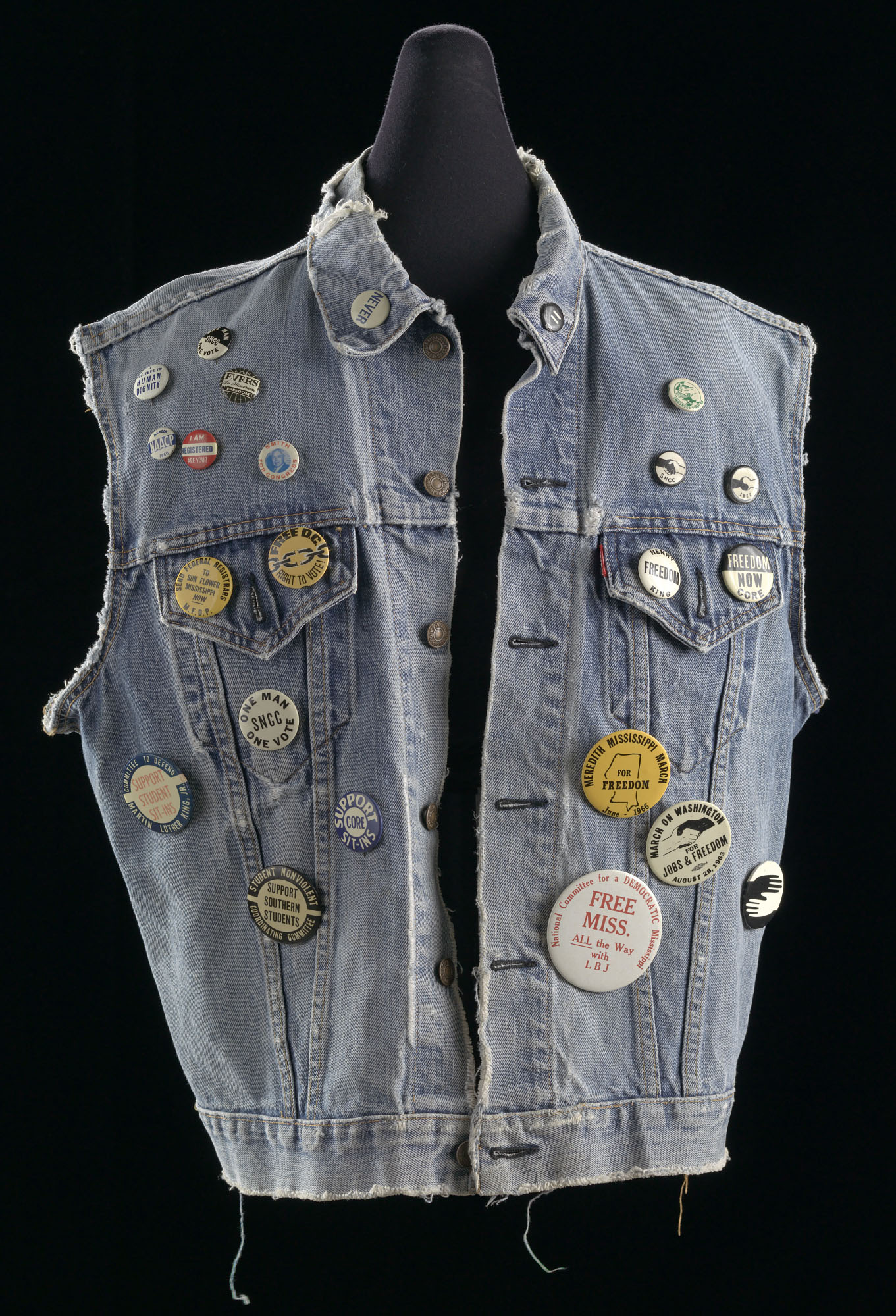 A denim vest worn by Joan Mulholland during the 1960s civil rights movement, covered with buttons advocating for social justice. 