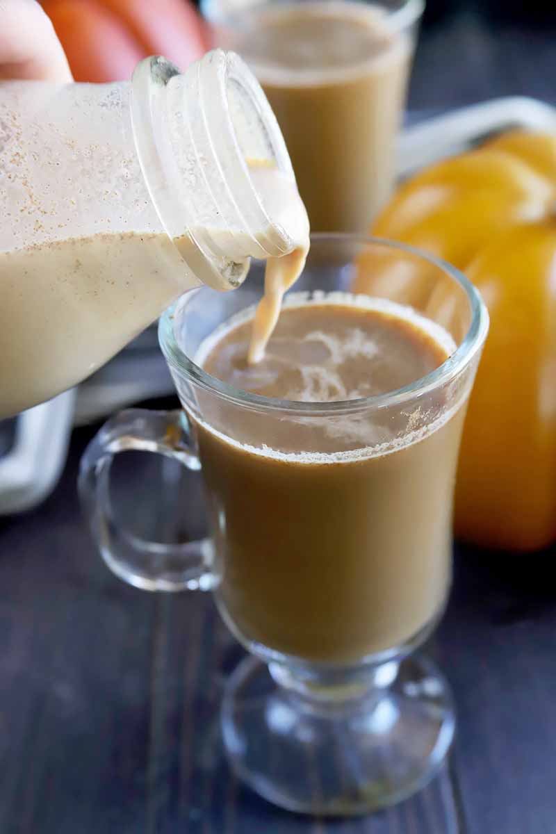 Vertical image of pouring a milky liquid into a glass of coffee.