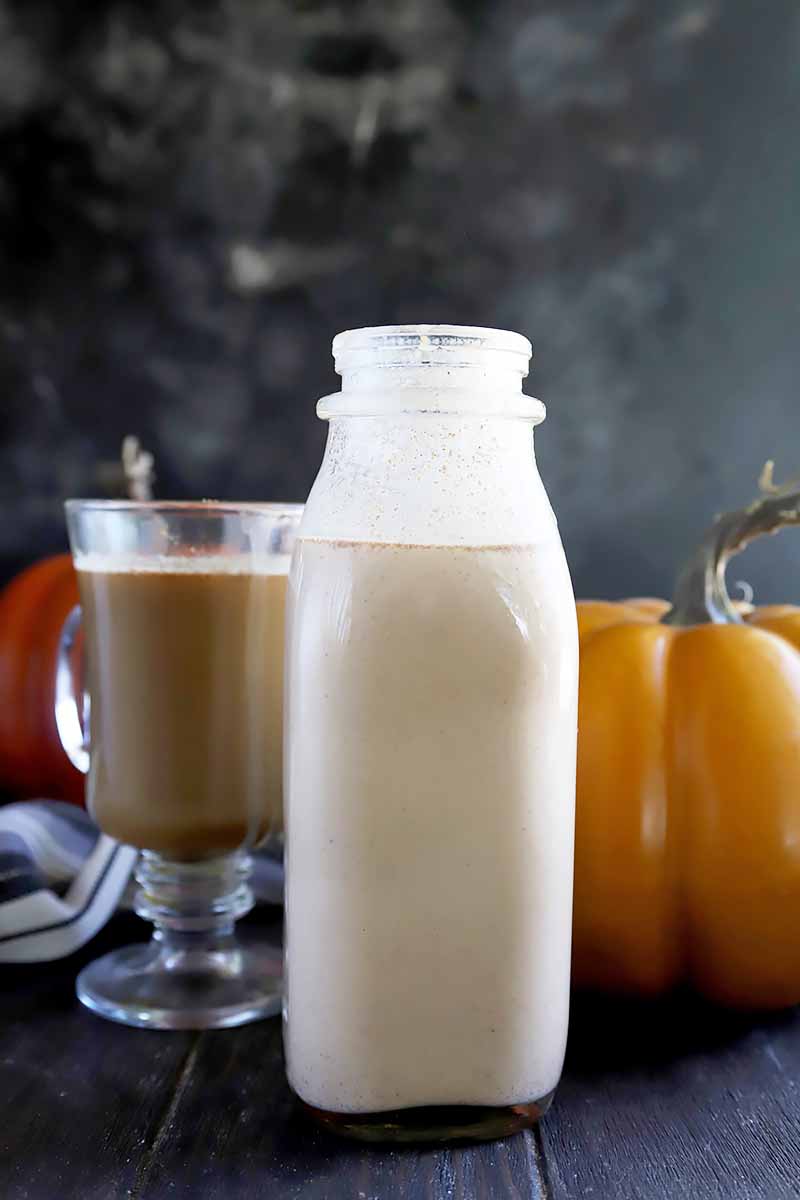 Vertical image of a bottle, a glass of coffee, and orange squash on a dark black background and surface.