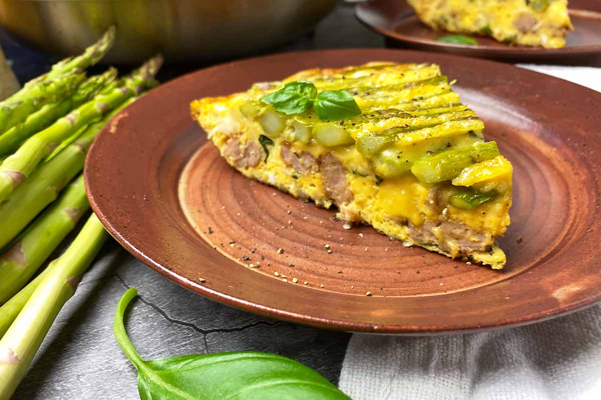 Horizontal close-up image of a wedge of vegetable and meat frittata on a brown plate.