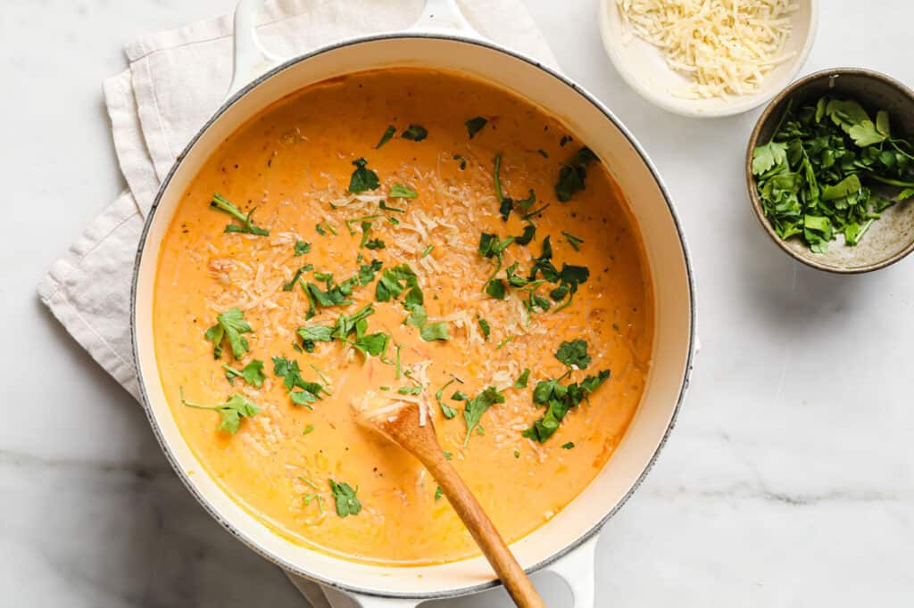 Creamy Italian sausage soup in a pot with a spoon and garnishes on the side.