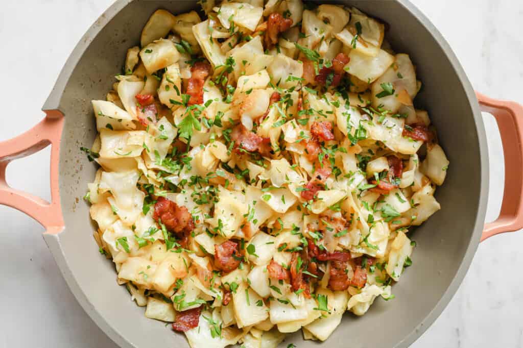 Fried cabbage with bacon garnished with parsley in a pot.