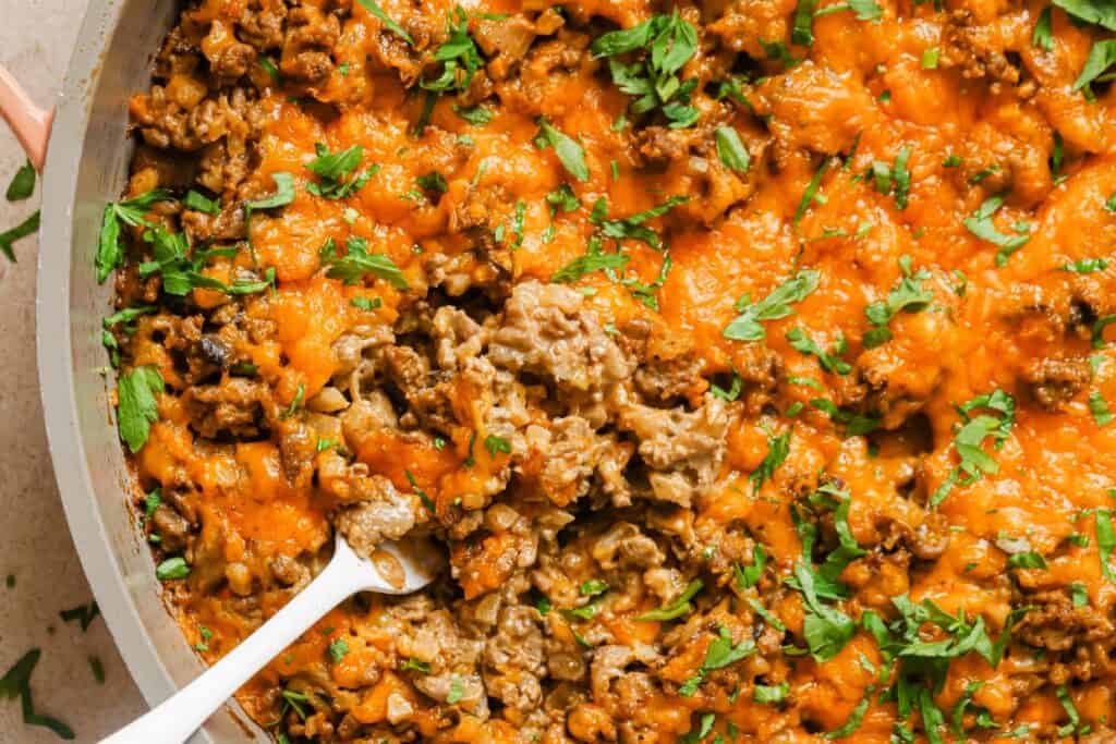 Creamy ground beef skillet with cauliflower rice garnished with fresh herbs with a fork.