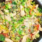 A skillet with vegetables and chicken in it.