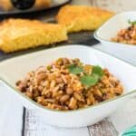 Bowl of hoppin' John on a white table with cornbread in the background.