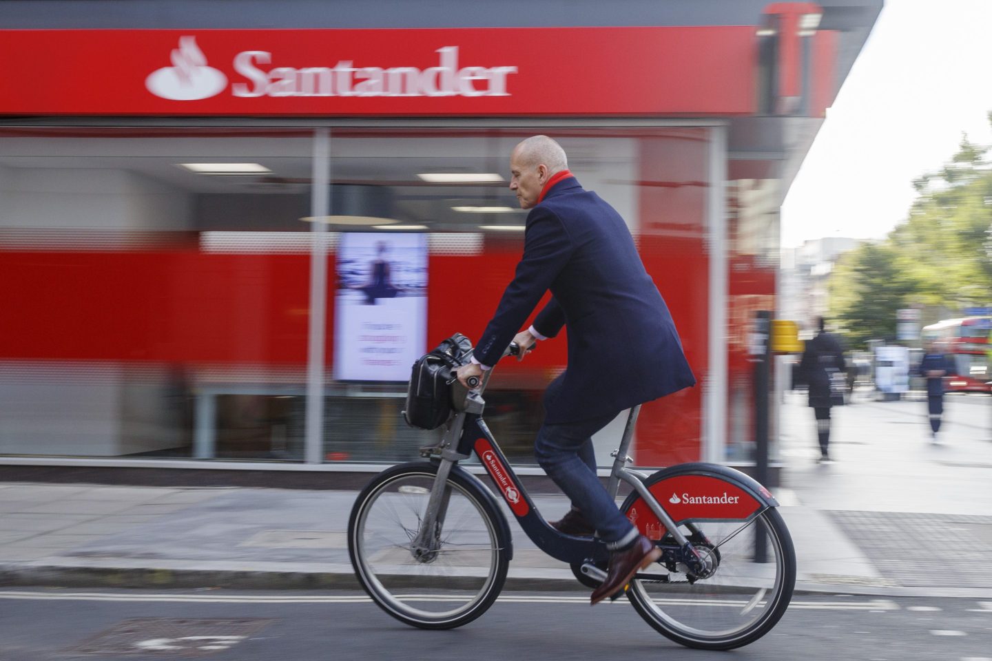 An office worker using a Santander Cycle hire bike travels passes a Banco Santander bank