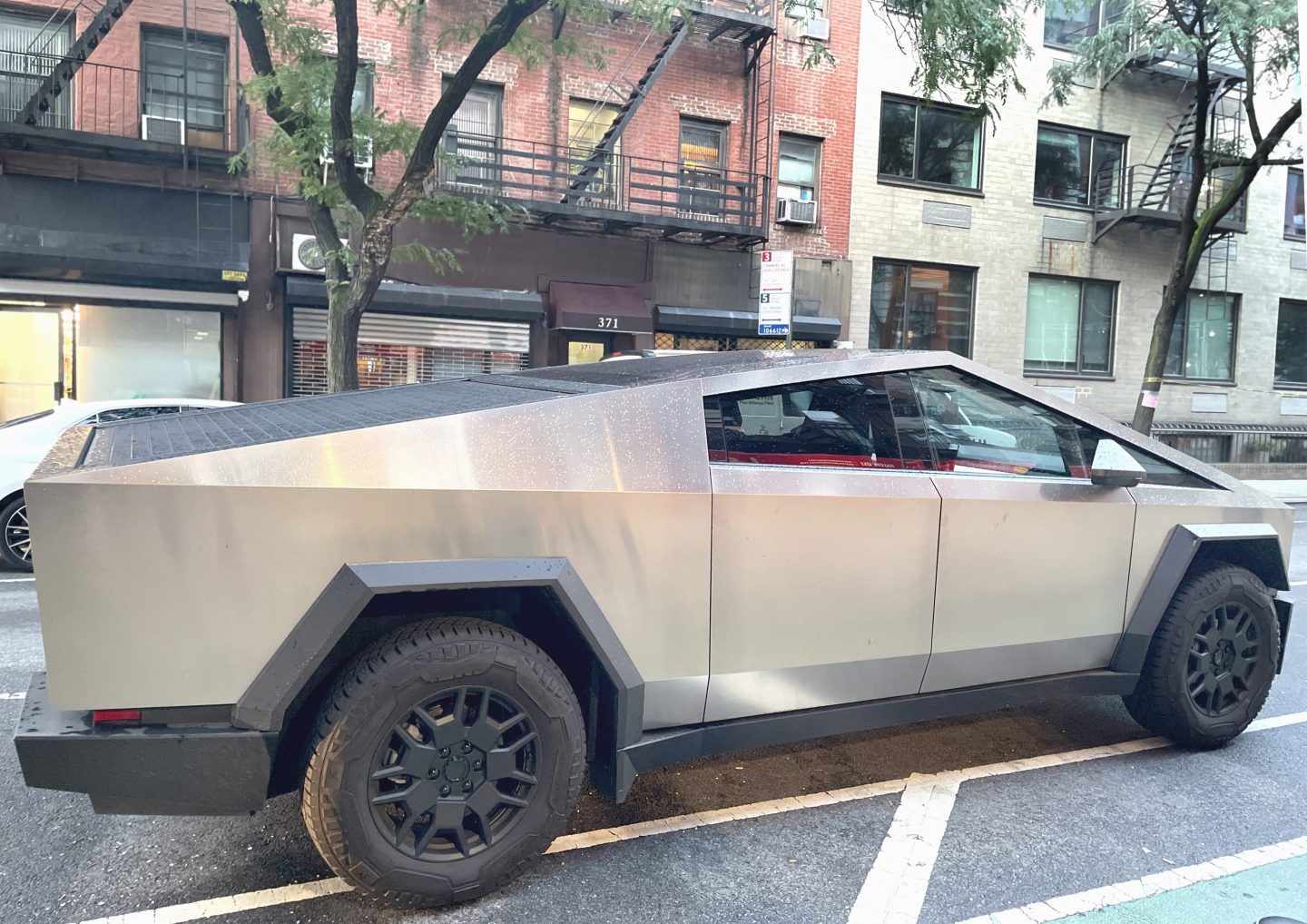 The Tesla Cybertruck parked on a New York City street after a rainstorm. This high-end vehicle is known for its durability and ruggedness, featuring shatter-resistant glass, a strong towing capacity, lockable storage, and a light bar for illuminating long distances. Inside, the Cybertruck is equipped with advanced technology, including a touchscreen interface..