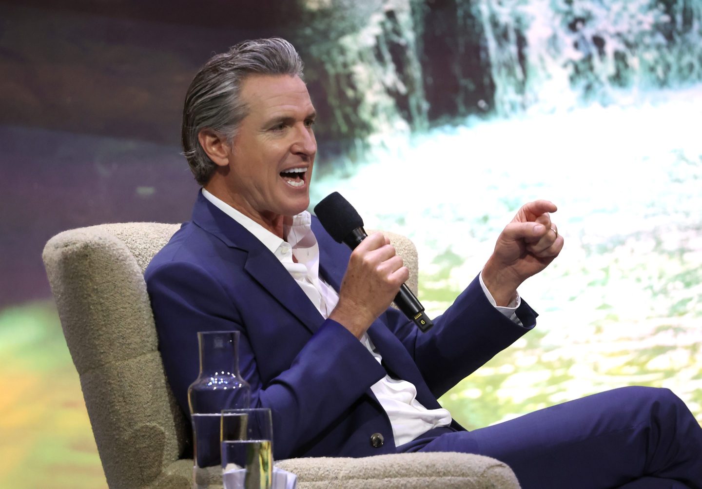 California Gov. Gavin Newsom sitting in a chair on stage and speaking into a microphone